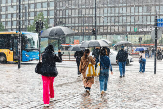 Ihmiset ylittävät katua sateenvarjojen kanssa Helsingin keskustassa rankkasateessa.